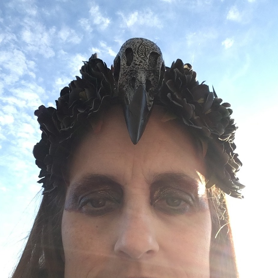 portrait of the artist in crow skull headdress, backlit by the sun