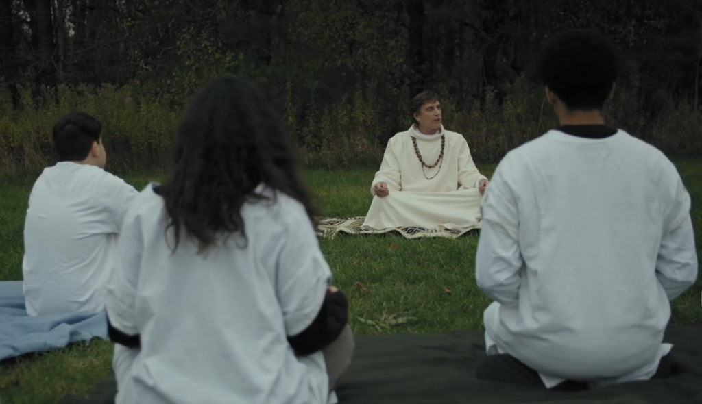A bunch of people wearing white sheets sitting in a semi-circle being talked at by an old white dude wearing white sheets. Web of Darkness picture.