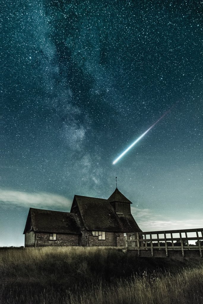 an old farm house with a meteor flying over it at night