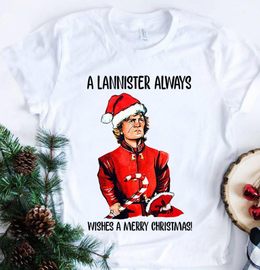 A white t-shirt with Tyrion Lannister wearing a red elf costume holding a candy cane. A Lannister Always Wishes a Merry Christmas is printed on the shirt with Tyrion.