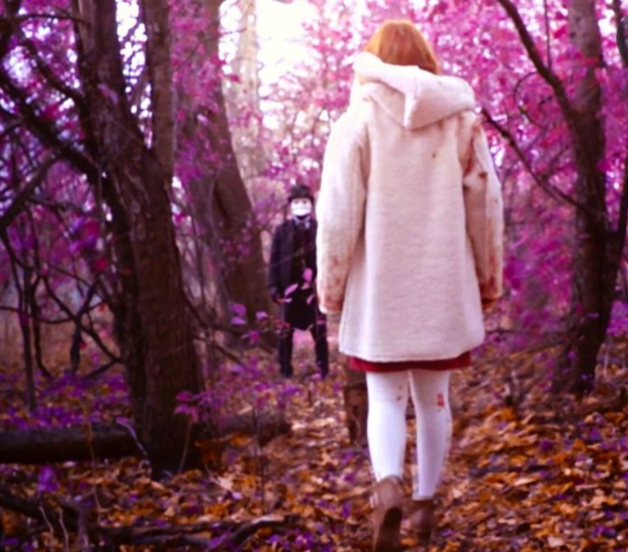 Slasher S4E7 a young woman in white walks through a purple woods towards what may be the killer