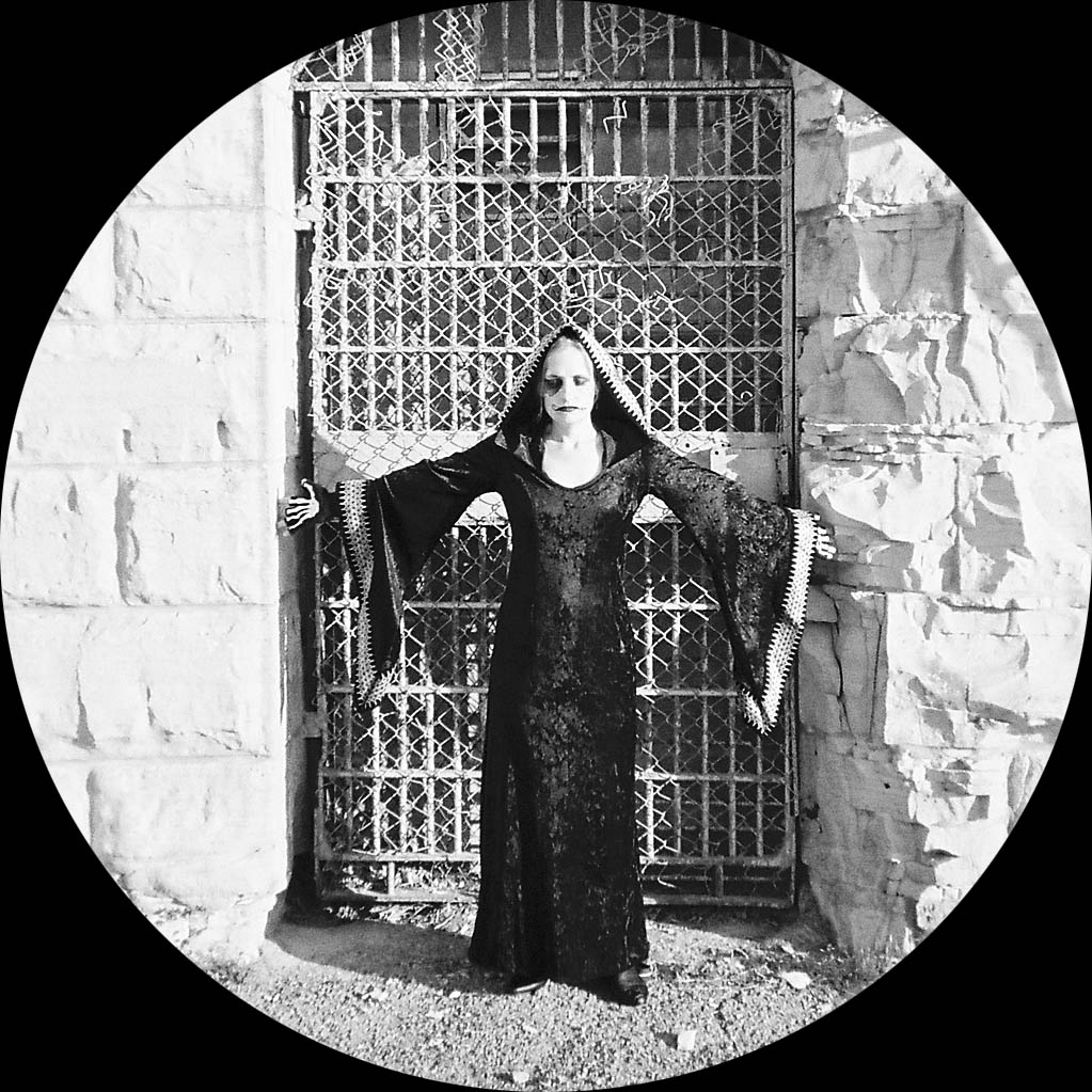 stark black and white photograph featuring ghoul with arms outstretched standing in front of metal gate