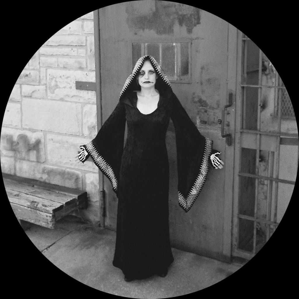 same ghoulish figure as photographed in front of a heavy metal door in black and white