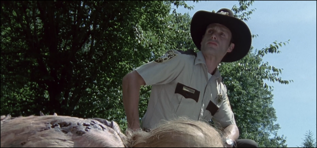 Screencap of The Walking Dead from The Last Drive-In with Joe Bob Briggs of Rick Grimes (Andrew Lincoln) looking pensively away from a zombie
