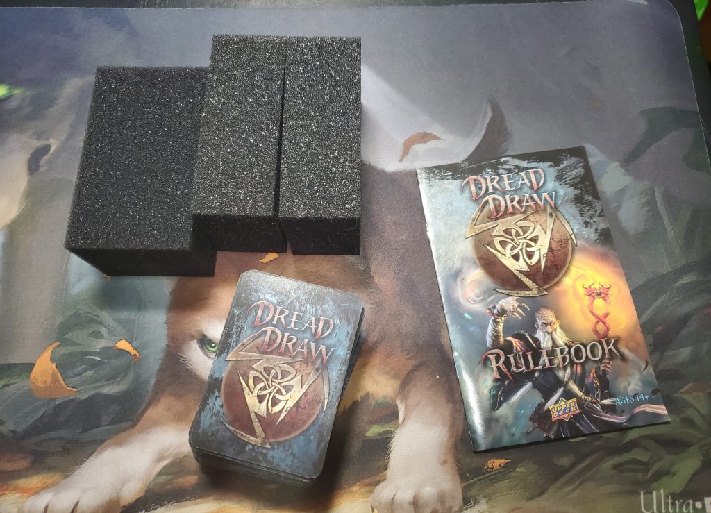 A photograph of the game's components taken out of the box. The foam blocks are in the top left, the card deck is in the bottom left, and the rule book is to the right.