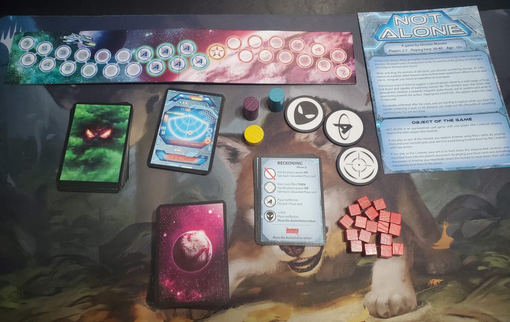 A photograph of the game's components laid out on a table. At the top is a long, thin board dotted with spaces. One half has a green and blue starry background, while the other has a pink and white planet background. To the right is the rulebook. Underneath the board is the hunt deck with green smoke and orange & yellow eyes, the survivor deck featuring a ship's console design, a short yellow token, a tall purple token, a tall blue token, and three black and white tokens. One of them has an alien design, one has an A with a horizontal loop around it, and one has a target symbol. Underneath these tokens is a deck of reminder cards, 18 red cubes, and a deck of place cards whose backing depicts a planet in space, all in a magenta hue.