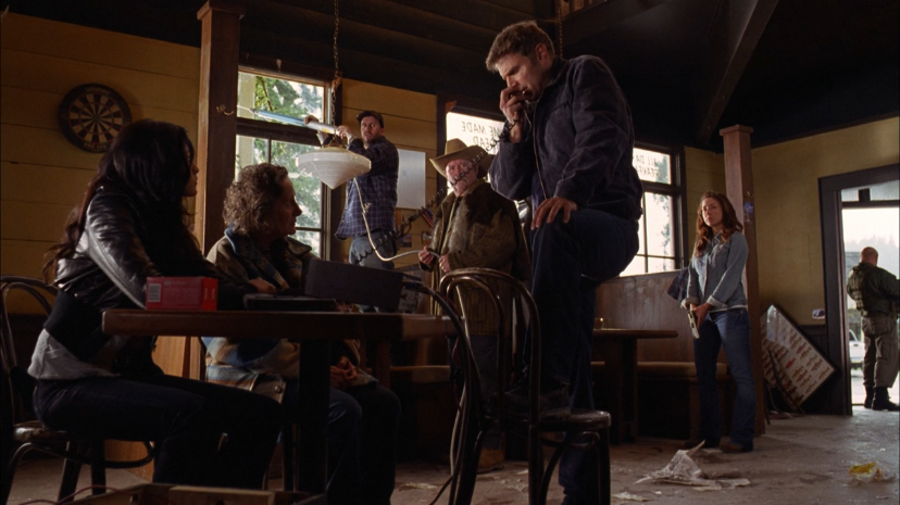 A photo depicting a scene from the film showing the main cast. From left to right, Tinsel Korey as Hampton is sitting at a table with Karen Elizabeth Austin as Edna beside her. Simon Longmore as Farley is holding an antenna out the window. Barry Corbin as Hass is holdin on to the wire connecting it to the radio. Nick Chinlund as Jake is in the center, talking into a CB radio. Off to the right is Erin Karpluk as Claire, and to the far right by the door is Don S. Davis as Colonel Sherman.