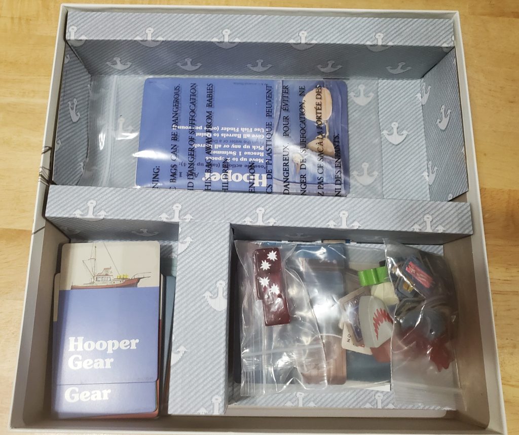 The components inside of the box. The cards fit loosely in the bottom left compartments, everything else besides the character boards fits in the bottom right compartment, and the character boards sit alone in the large top compartment.