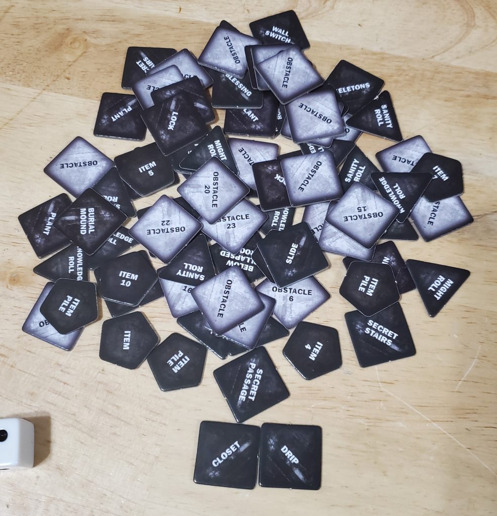 A pile of assorted tokens in various shapes. Some are dark grey with white text and others are light grey with black text.