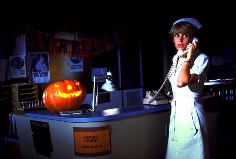 A nurse is standing on the right of the picture, she's on the phone, looking worried. There is a light orange pumpkin on the desk