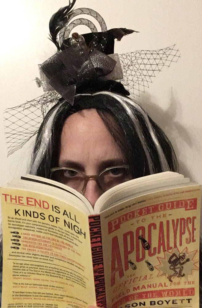 Reviewer Jennifer Weigel reading Pocket Guide to the Apocalypse: image of myself with white streaked black hair and miniature top hat peering over the top of the book by Jason Boyett