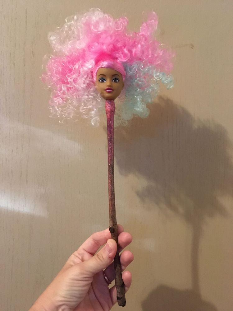 A finished fairy wand, ready to conjure wishing magic... image features a hand holding a fairy head with curly pink, blue and white hair on a stick