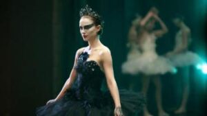 Black background, a young woman is dressed as Black Swan looking away from the camera. A woman dressed in white whose face we can't see is in the back of the image