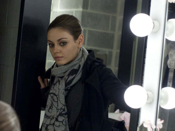 A brunette woman dressed in a coat in scarf is standing in the doorway looking at someone out of view.