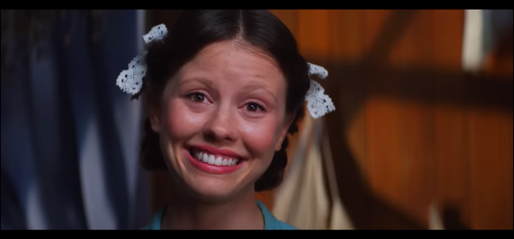 Screenshot from 'Pearl' of Mia Goth as Pearl, staring at the camera with a pained smile.