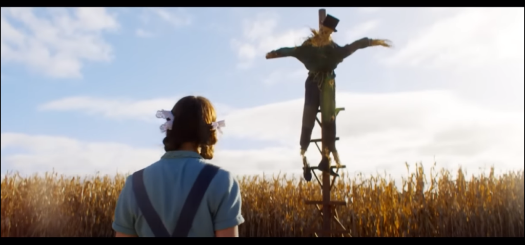 Screenshot from 'Pearl' of Mia Goth as Pearl, looking at an unnerving scarecrow.