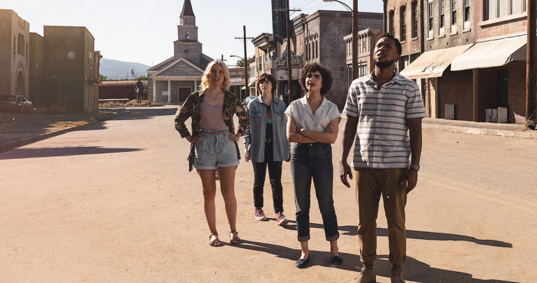 Characters Melody, Lila, Ruth, and Dante standing together observing an object off camera. Dante's hands resting at his sides wearing a blue and white striped polo shirt in brown pants. Short curly brown-haired Melody stares up, arms crossed below her chest in a white collard-button shirt and blue jeans. Their friend Ruth observers, hands gripping at the waist. Her hair is wavy blonde. Outfit, light denim shorts with a printed black cardigan draped over a faded purple shirt. Lila stands in the back, short brown hair rests over her right eye. She stands bored, hands resting at her sides. Her outfit feeling the warmest of all under the blazing sun as she wears a denim jacket over a black graphic tee. Her pants tight and black, strutting in her dirty red converse. 