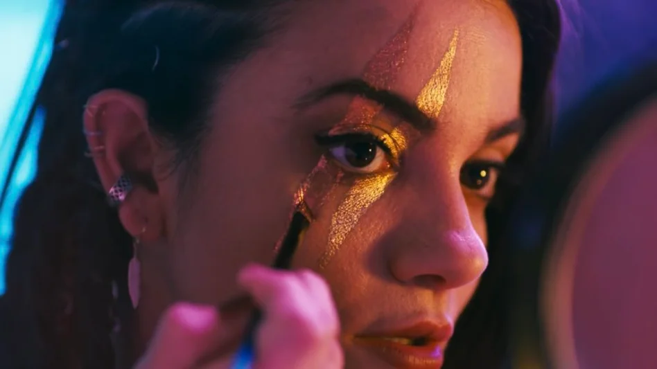 Laruern LaVera as Sienna Shaw applying gold makeup in streaked pattern across her right eye. Image from Terrifier 2.