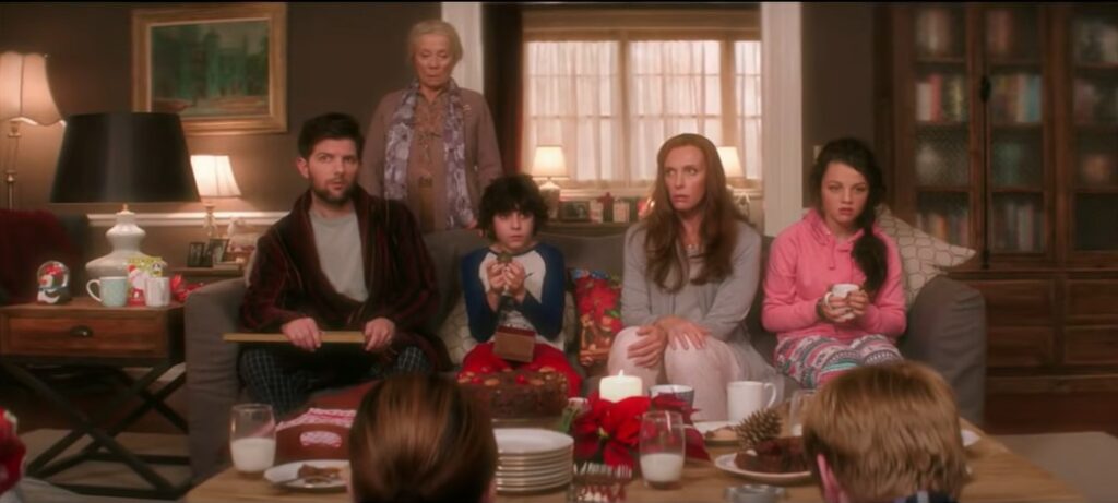 an image of Max and his family sitting on a couch. Looks of dread paint theirs faces as they recall the events of Christmas Eve. Max's father Tom is wrapped in a fleeced robe with pine green plaid pajama bottoms covers his legs. Protagonist max sits in a blue and white baseball tee cradling a rusted jingle bell gifted to him by Krampus. Max's mother Sarah is drapped in a grey cardigan and white sweat pants, her hands nervously resting on her legs. Beth is seen in the most colorful wardrobe of the family. A bright pink hoodie covers her torso, as her legs are warmed in festive purple, blue, pink and white printed leggings, tensely gripping her mug of hot liquid. Omi protectively hovers above her family, a look of sorrow washing over her as she stares at the bell in Max's hands. A purple floral scarf loosely rests on her neck and relax-fitted button shirt. The scene is lighted with an eerie  ominous glow. 