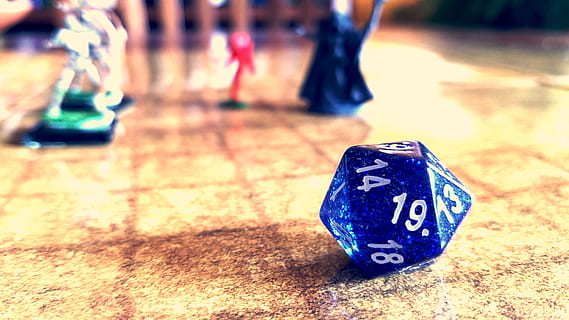 A 20-sided die on a game mat with three miniatures in the background