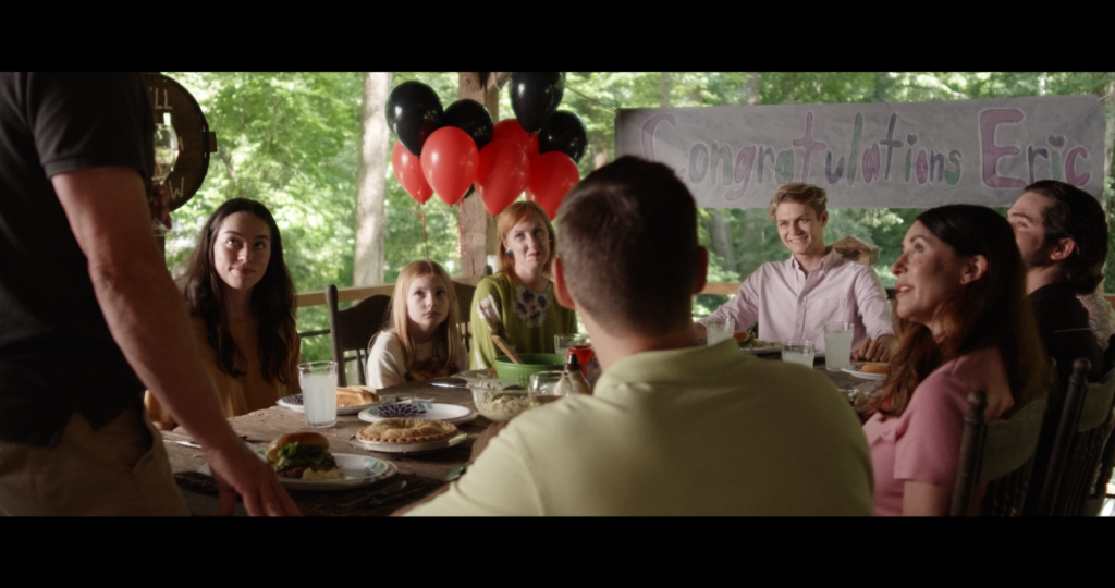 A party celebrating a young man. Behind the young man is a sign of Congratulations. He is surrounded by friends and family in an outside patio.