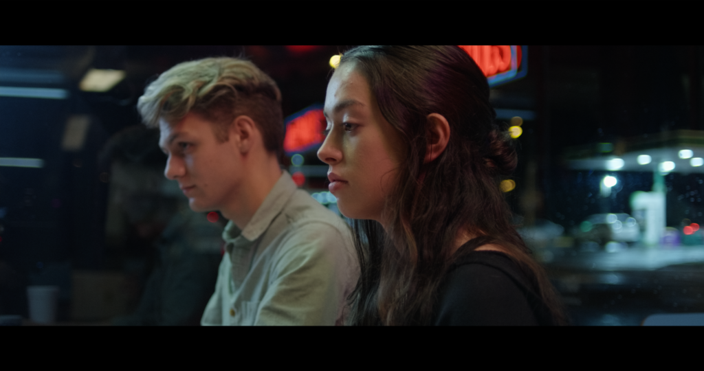 Boy and girl sitting next to each other at night. Neon lights in the distance