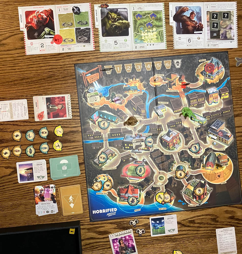Horrified Game Setup with board, players (Journalist and Cryptozoologist), monsters (Mothman, Ozark Howler and Bigfoot), cards and item/monster tokens