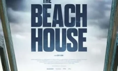 "The Beach House" stated directly in the middle of the poster. Above is a stormy sky, below is the beach with a woman poking her head above a staircase.
