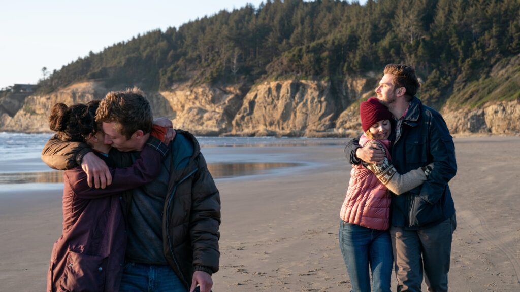 Two couples some distance apart at the beach. Each couple holding their significant other.