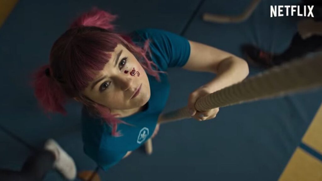 A woman with pink hair climbing a rope, blood dripping on her face.
