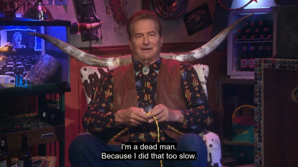 Joe Bob Briggs sits in his longhorn chair and demonstrates how to tie a one-handed bowline knot. The caption on the image reads "I'm a dead man. Because I did that too slow."