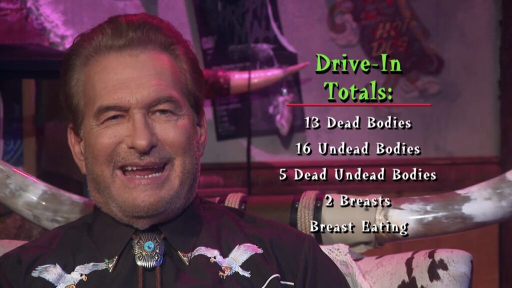 Joe Bob reads the Drive-In totals for Manchester. The text on the screen reads: 13 dead bodies, 16 undead bodies, 5 dead undead bodies, 2 breasts, breast eating.