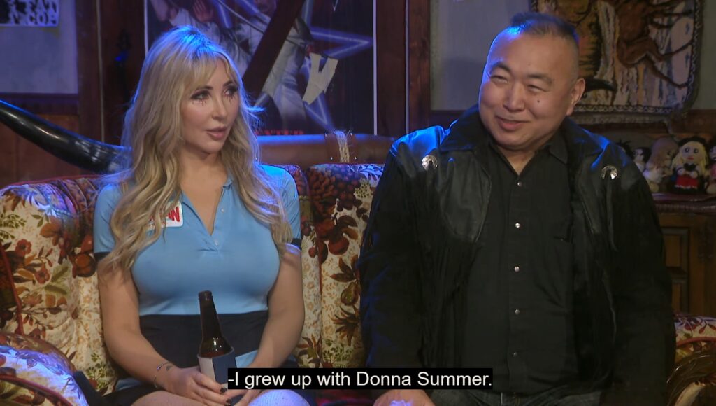 Yuki Nakamura sits next to Darcy the Mail Girl on the interview couch. He is saying "I grew up with Donna Summer."