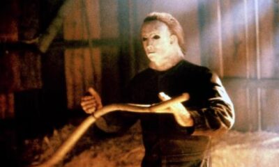 Michael Myers from Halloween is holding some sort of gardening tool and looking at something off-camera.