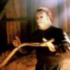 Michael Myers from Halloween is holding some sort of gardening tool and looking at something off-camera.