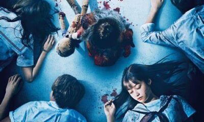 Six students lying on a white floor looking like they are asleep. A girl in the middle, standing over them with a stuffed animal. The little girl's footsteps leave bloody imprints.