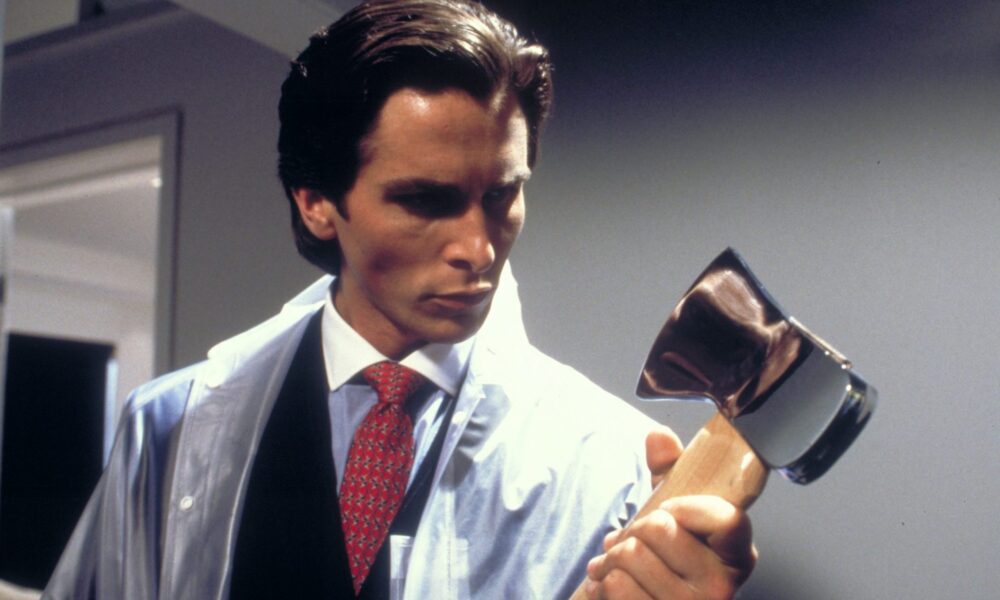 Patrick Bateman is holding an axe looking down on it while holding it in his arms. He's wearing a seethrough coat on top of a business suit.