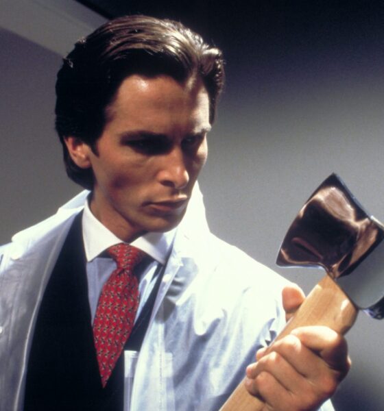 Patrick Bateman is holding an axe looking down on it while holding it in his arms. He's wearing a seethrough coat on top of a business suit.