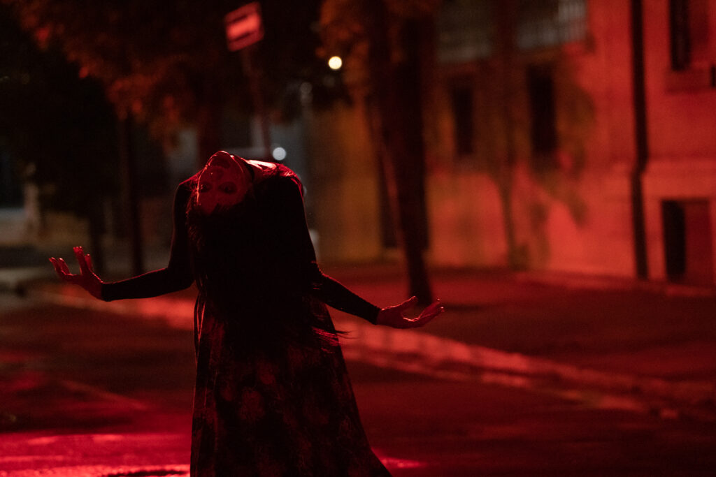 A woman bends backward to look over at someone. The street she's on is red and ominous.