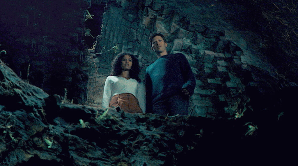 A woman and a man look down at a mysterious cave.