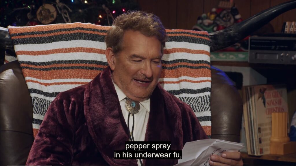 A still image from Joe Bob's Creepy Christmas. It shows Jow Bob in his blanket adorned long-horn chair reading from the first letter of the night.