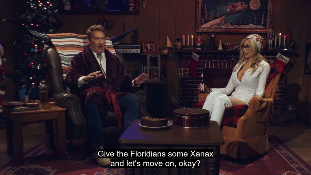 A still image from Joe Bob's Creepy Christmas. It shows Joe Bob and Darcy sitting in a room decorated for Christmas. The captioning reads, "Give the Floridians some Xanax and let's move on, okay?"