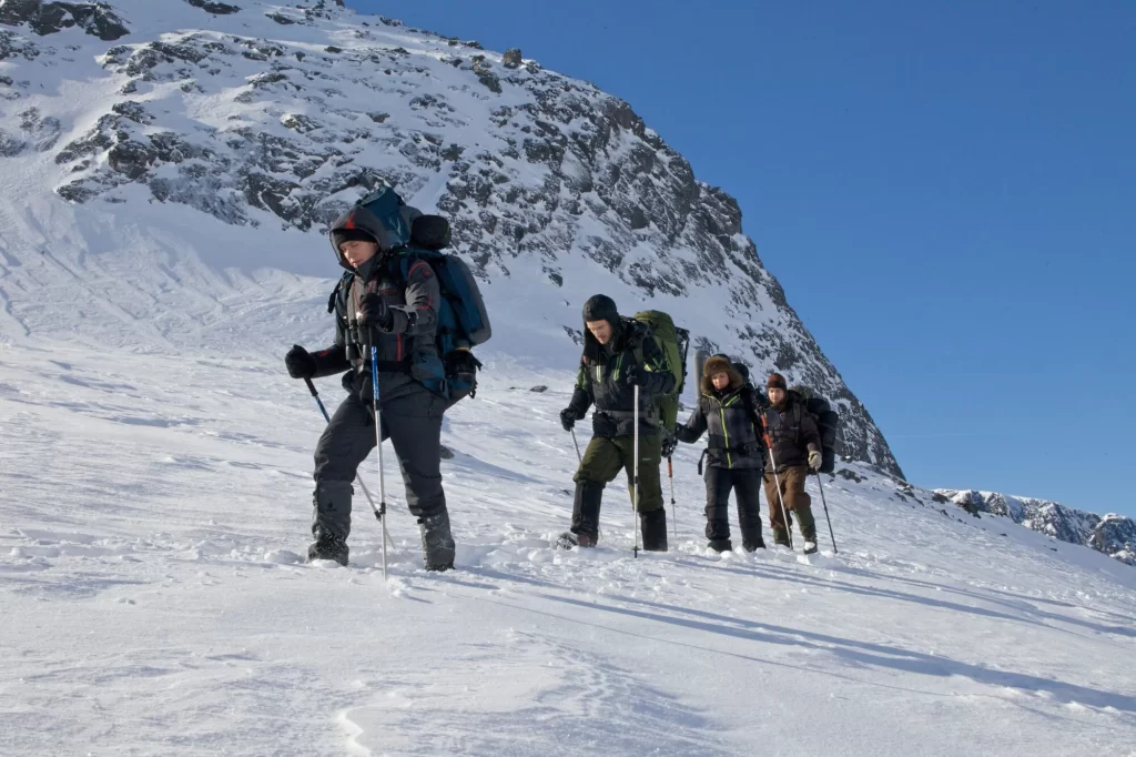 Four hikers travel up a snowy mountain slope in the middle of the day.