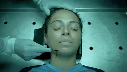 A woman lays on an autopsy table with a person cutting her face