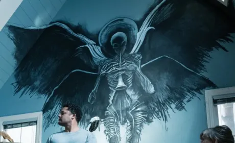 A winged creature painted on a wall, emerging from the dark etchings around it. On its chest rests a trumpet