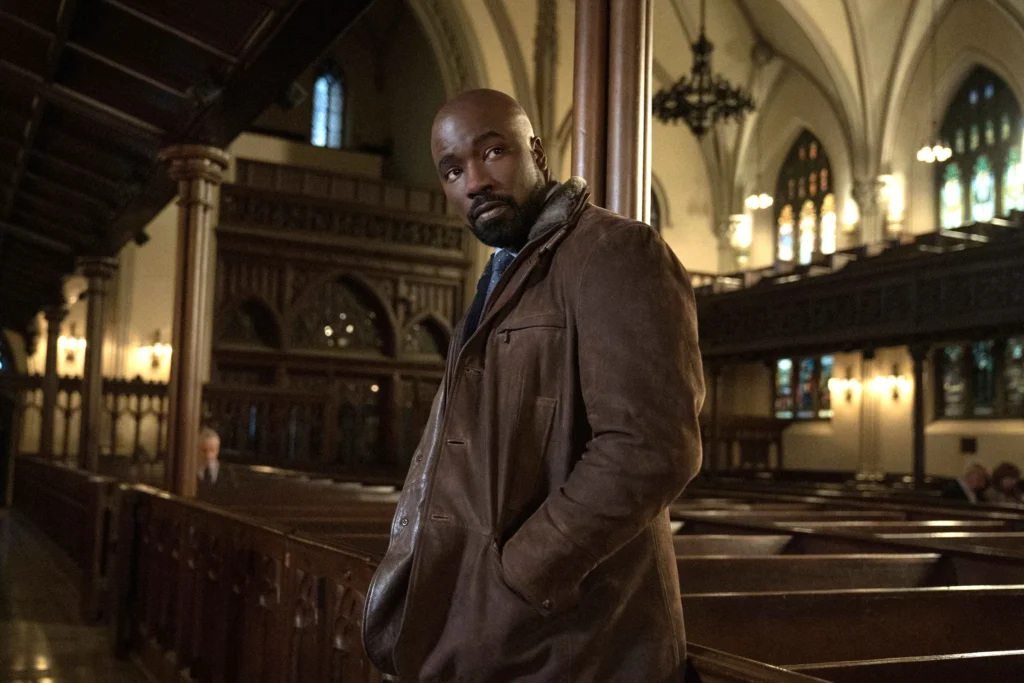 A man leans on a pew in a church. He seems to look around, cautious of who's around