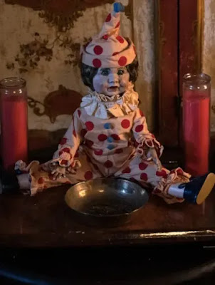 A doll in a clown outfit sits in the middle of a shrine.