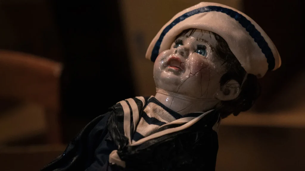 A doll in a sailor outfit that looks decrepit. Behind him is a room.