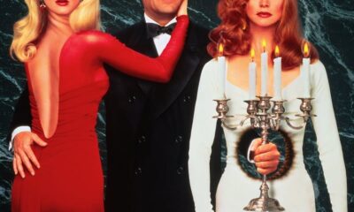 A woman in red looks at the viewer with her head turned around. Another woman stands in the other side of a man with a hole in her dress. A man holds a candle through the hole in the woman in white.