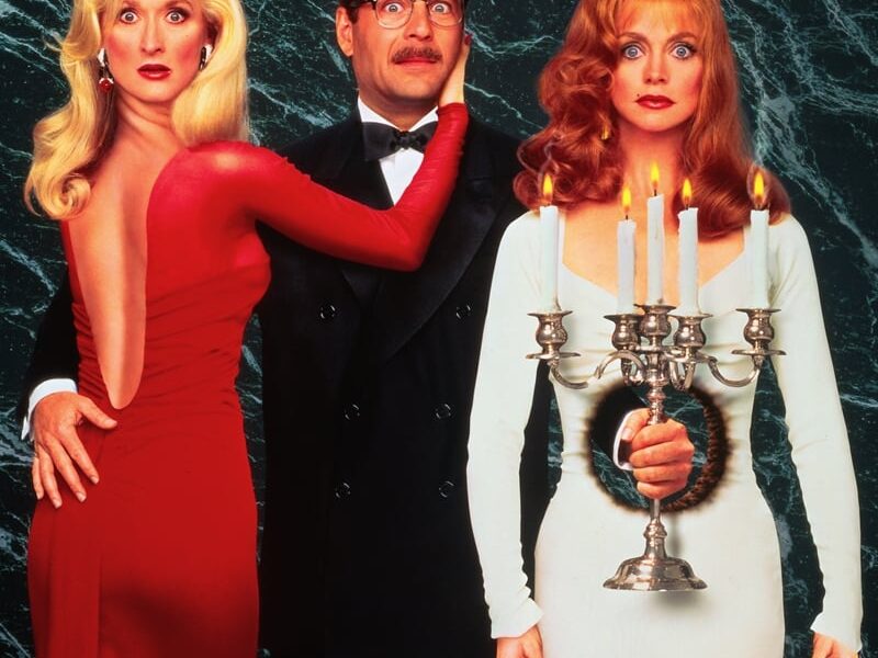 A woman in red looks at the viewer with her head turned around. Another woman stands in the other side of a man with a hole in her dress. A man holds a candle through the hole in the woman in white.